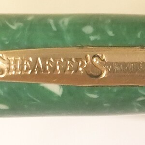May include: Close-up of a green pen with a gold band that reads "Sheaffer's".