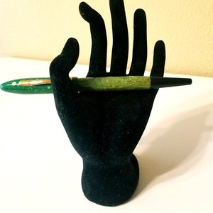 May include: A green and black fountain pen with gold accents on a black velvet hand stand.
