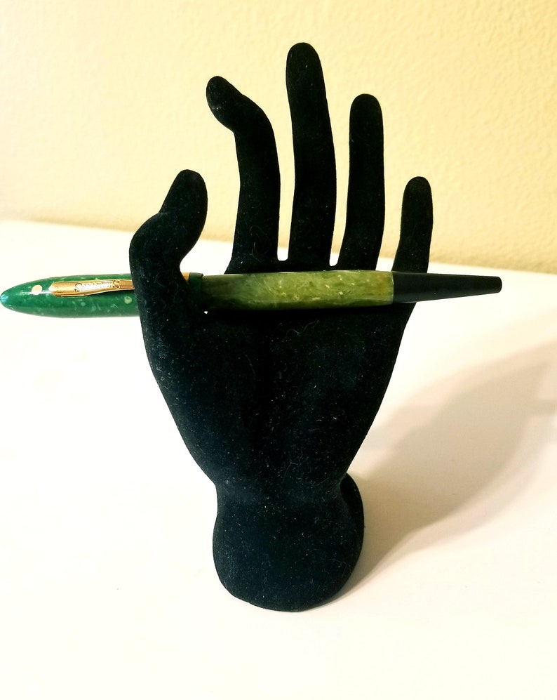 May include: A green and black fountain pen with gold accents on a black velvet hand stand.
