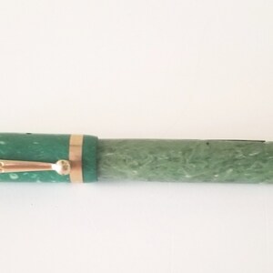 May include: A green and gold fountain pen with a marbled pattern. The pen has a gold trim and a black cap.