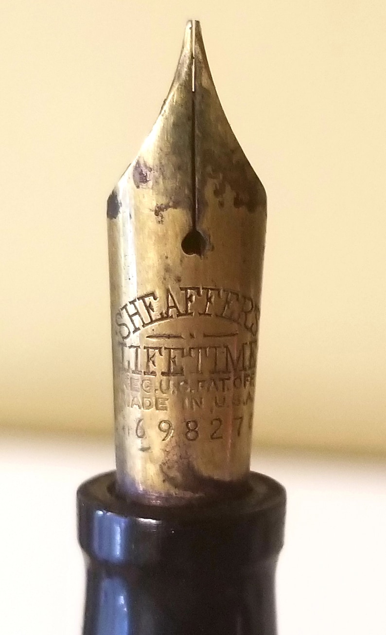 May include: Close-up of a gold-toned fountain pen nib with the inscription "Sheaffer's Lifetime Reg. U.S. Pat. Off. Made in U.S.A. 169827".