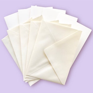 May include: A fan of cream-colored envelopes, each with a triangular flap. The envelopes are arranged on a light purple background. The paper appears to be smooth and opaque, suitable for various correspondence needs.