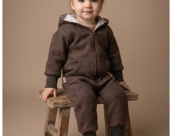 May include: A dark brown hooded jumpsuit featuring a front zip closure, long sleeves with ribbed cuffs, and a floral patterned lining inside the hood. The garment has a kangaroo pocket on the front and ribbed leg cuffs, providing a full-body fit.