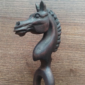 Peut inclure: Un bâtonnet à cheveux en bois brun foncé en forme de tête de cheval. La tête de cheval est sculptée avec des détails et a une crinière. Le bâton est long et fin.