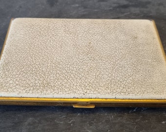 Puede incluir: Un estuche de cigarrillos vintage con ribete dorado y un exterior de cuero blanco texturizado.
