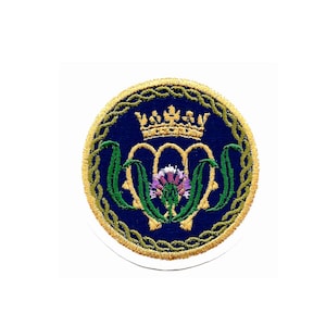 May include: A gold embroidered patch with a blue background. The patch features a crown, a thistle, and a Celtic knot design.