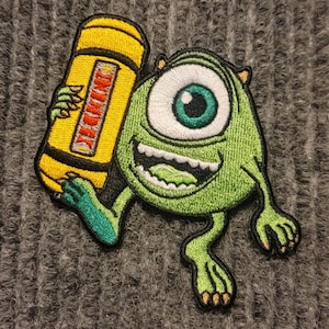 May include: Green one-eyed monster cartoon character holding a yellow crayon. The monster is smiling with a large mouth and has three toes on each foot.