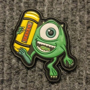 May include: A green one-eyed monster cartoon character holding a yellow can with the word "remarkable" printed on it. The character has a toothy grin and is wearing black shoes.