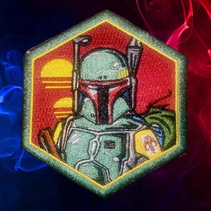 Op de afbeelding: Geborduurd zeshoekig embleem met Boba Fett uit Star Wars. De patch heeft een groene rand. Boba Fett wordt afgebeeld in zijn groene en rode harnas, tegen een rode achtergrond met een gestileerde zonsondergang.