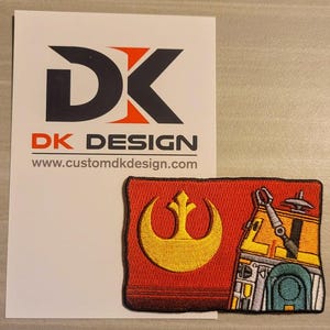 May include: A red embroidered patch with a yellow Rebel Alliance symbol and a depiction of a droid. The patch is on a white background with a business card that says "DK DESIGN" and "www.customdkdesign.com".