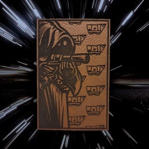 May include: A brown leather patch featuring a detailed illustration of a robed figure holding a telescope, with a series of stylized vehicles on the right. The background is a black space-themed design with white streaks.