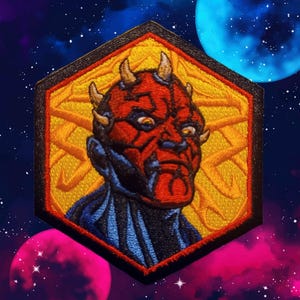 May include: Embroidered patch featuring a red-faced character with horns, set within a gold and black hexagonal frame. The character has a stern expression and is set against a cosmic background with planets and stars. The patch is likely for clothing or accessories.