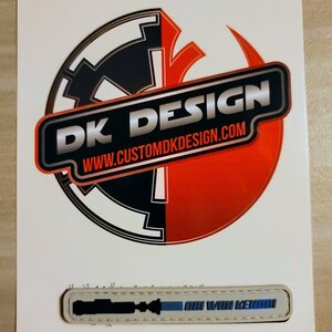 May include: A white card with a black and red logo that says "DK DESIGN" and "www.customdkdesign.com". Below the logo is a beige patch with a black silhouette of a lightsaber and the text "OBI WAN KENOBI" in blue.