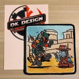 May include: Embroidered patch featuring a green and brown Star Wars character, Boba Fett, with a blue and red character, a bounty hunter, in a desert setting. The patch has a black border and the text "DK DESIGN www.custo.com".