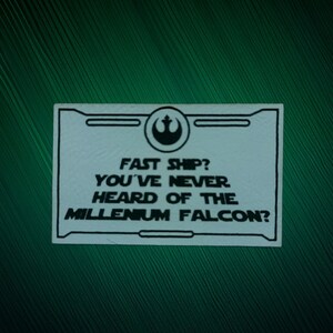 Könnte beinhalten: Ein weißer rechteckiger Aufkleber mit schwarzem Text und einem Star Wars Rebel Alliance-Symbol. Der Text lautet: "FAST SHIP? YOU'VE NEVER HEARD OF THE MILLENIUM FALCON?" Der Aufkleber befindet sich auf einem dunkelgrünen Hintergrund.
