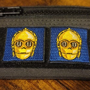 May include: A black zippered pouch with two embroidered patches featuring a yellow C-3PO character from Star Wars.