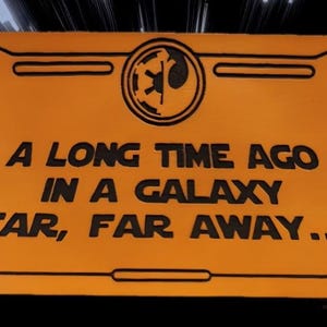 May include: Orange rectangular sign with black border and text: "A LONG TIME AGO IN A GALAXY FAR, FAR AWAY..." Features a black and white emblem in the upper center. The background has a blurred, streaking effect.