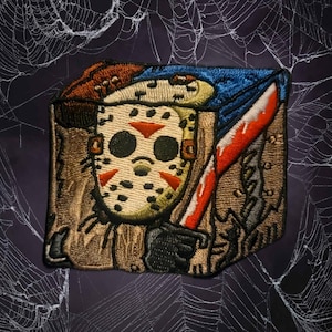 May include: Embroidered patch featuring a hockey mask with red triangles, a bloody knife, and a brown and blue color scheme. The patch has a textured appearance and is likely for clothing or accessories.