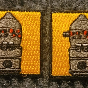 May include: Two embroidered patches featuring a robot with red eyes and a yellow background.