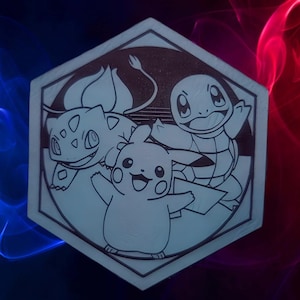 May include: A light-colored, hexagonal coaster featuring engraved images of Pikachu, Bulbasaur, and Squirtle. The characters are outlined in black, with a light background. The coaster has a beveled edge and is set against a gradient background of blue and red.
