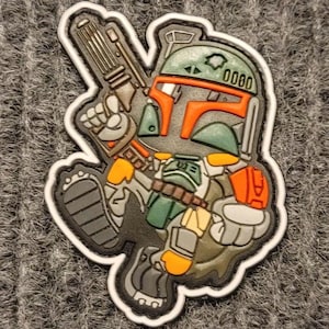 May include: A green and orange cartoon Boba Fett character with a blaster rifle, wearing a helmet with the number 0000 on it. The character is standing on a white background.