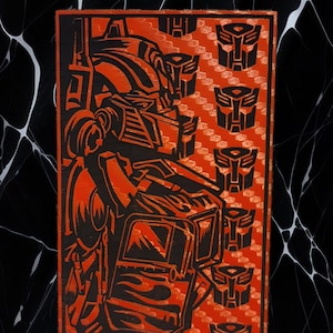May include: An orange and black artwork depicting a robot character. The design includes the robot's face and body, with several robot head symbols on the right. The artwork is set against a black and white background.