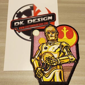May include: Embroidered patch featuring C-3PO from Star Wars, in gold and cream colours, set against a pink and black background. The patch includes a red and yellow symbol and the text "DK DESIGN" and "www.customdkdesign.com".