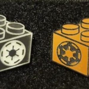 May include: Two Lego-style pins, one white and one orange, each featuring the Star Wars Imperial symbol.