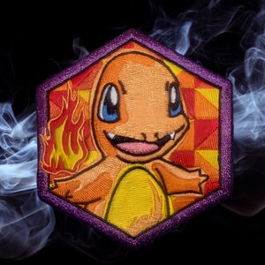 May include: Embroidered patch featuring Charmander, an orange and yellow fire-type Pokémon. The patch has a purple hexagonal border and a colorful background. The design includes flames and a smiling Charmander.