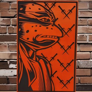 May include: Orange and black wall art featuring a side profile of a ninja turtle with a determined expression. The artwork includes several black sai weapons on an orange background, set against a brick wall.