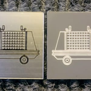 May include: Two metal plates with a laser-etched image of a small, boxy vehicle with a grid pattern on the side. The vehicle has four wheels and a flat roof. The image on the left plate is in gray, while the image on the right plate is in white.