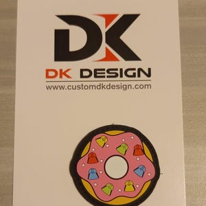 Könnte beinhalten: Ein rosafarbener und gelber Donut mit bunten Streuseln. Der Donut befindet sich auf einem weißen Hintergrund mit dem Text "DK DESIGN" und "www.customdkdesign.com".