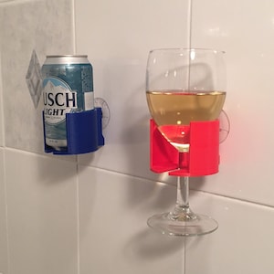 May include: Two suction cup holders for a glass and a can. The glass holder is red and the can holder is blue. A glass of white wine is in the glass holder and a can of Busch Light is in the can holder.