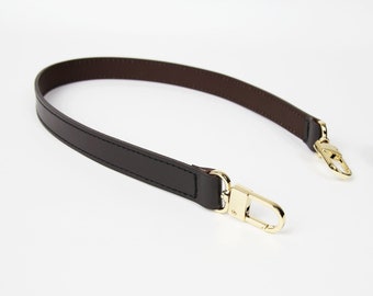 May include: A brown leather strap with gold metal clasps. The strap is approximately 100 cm long.