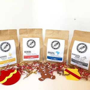 May include: Four bags of coffee beans with festive holiday decorations. The bags are labeled with the origin of the beans: Colombia, Kenya, Brazil, and Dominion Dark.