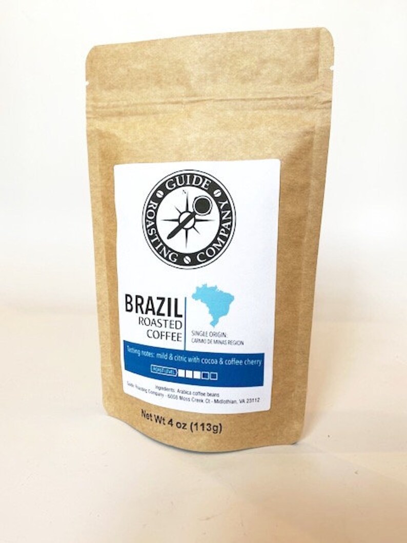 May include: A brown paper bag with a white label that says "Guide Roasting Company" and "Brazil Roasted Coffee". The label also includes a compass logo, a map of Brazil, and tasting notes. The bag contains 4 ounces (113 grams) of coffee.