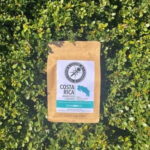 May include: A brown paper bag with a label that says "Costa Rica Roasted Coffee". The label also includes the origin of the coffee beans, which is "Tarrazu,  small coffee farms in San Jose, Costa Rica". The label also says "Tasting notes: sweet cocoa with prune & citrus fruit". The bag is 12 ounces (340g).