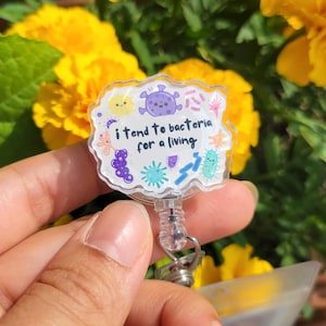 May include: A clear plastic badge holder with a colorful cartoon design featuring bacteria and the text "i tend to bacteria for a living".