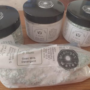 May include: Three jars and a bag of Goat Milk Detergent. The jars have black lids with a white label and the text "Midnight Water". The bag has a clear plastic with a white label that reads "Goat Milk Detergent".