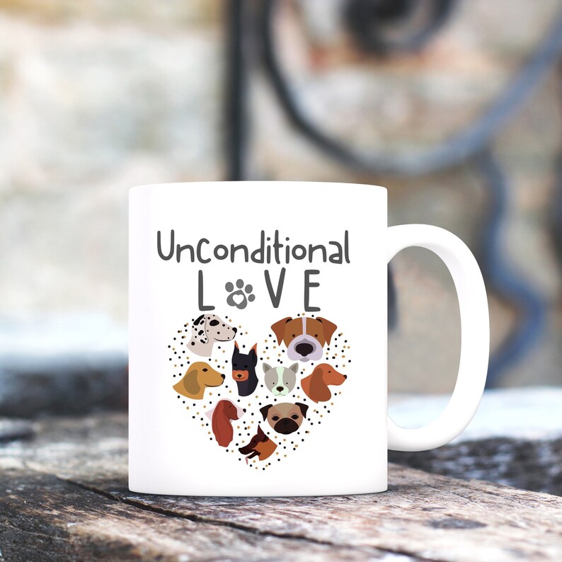 May include: White ceramic coffee mug with a black and brown illustration of dog faces in a heart shape. The text "Unconditional LOVE" is printed on the mug.