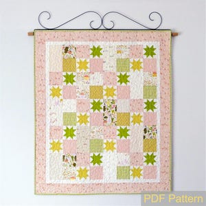 May include: A handmade quilt with a pink, white, and green color scheme. The quilt features a star pattern with green and yellow stars, and squares of pink, white, and patterned fabric. The quilt is hanging from a decorative metal rod.