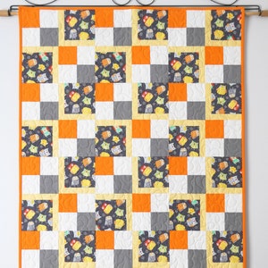 May include: A patchwork quilt with squares of orange, white and grey fabric. Each square features a different pattern of owls. The quilt is hanging on a wall with a decorative rod.