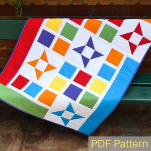 May include: A colourful quilt with a white background and a variety of geometric shapes, including squares and stars. The quilt is made with fabrics in shades of red, orange, yellow, green, blue, and purple. The quilt is folded and displayed on a wooden bench. The text "PDF Pattern" is visible at the bottom of the image.