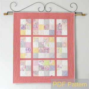 May include: A pink and white patchwork quilt with a floral pattern. The quilt is hanging on a wall with a black metal rod. The quilt is framed with a coral border. The text "PDF Pattern" is printed at the bottom of the image.