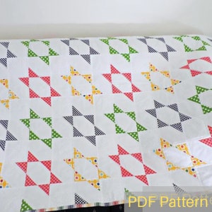 May include: A white quilt with a repeating pattern of red, yellow, green, and blue stars. The quilt is made with a variety of fabrics with different patterns. The quilt is on a white surface. PDF Pattern