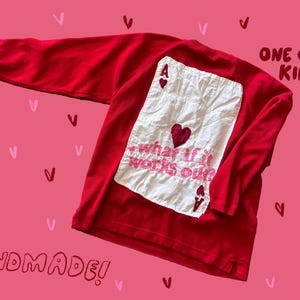 May include: A red long-sleeved shirt with a white patch featuring a playing card design and the embroidered phrase "what if it works out?". The words "ONE OF A KIND!" and "HANDMADE!" are also visible.