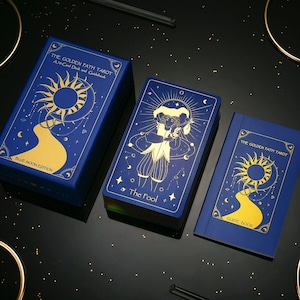 Pode incluir: Uma caixa de baralho de tar&ocirc; azul e dourado com o t&iacute;tulo "The Golden Path Tarot" e o texto "A 78-Card Deck and Guidebook". A caixa tamb&eacute;m tem o texto "Blue Moon Edition". Um &uacute;nico cart&atilde;o de tar&ocirc; com o t&iacute;tulo "The Fool" &eacute; vis&iacute;vel. Um guia azul e dourado com o t&iacute;tulo "The Golden Path Tarot" tamb&eacute;m &eacute; vis&iacute;vel.