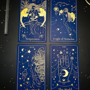Pode incluir: Quatro cartas de tar&ocirc; com designs em folha de ouro sobre um fundo azul escuro. As cartas s&atilde;o Temperan&ccedil;a, Cavaleiro de Pent&aacute;culos, A Estrela e O Mundo.