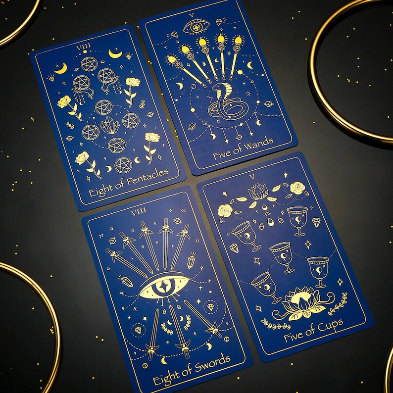 Pode incluir: Quatro cartas de tar&ocirc; com desenhos de folha de ouro em um fundo azul escuro. As cartas s&atilde;o: Oito de Pent&aacute;culos, Cinco de Paus, Oito de Espadas e Cinco de Copas.