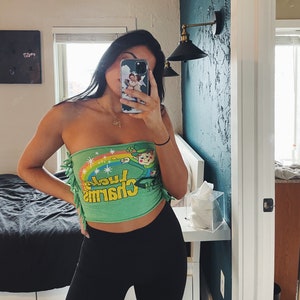 May include: A green tube top with a graphic of a leprechaun and the text "Lucky Charms". The top has a rainbow and stars on it.